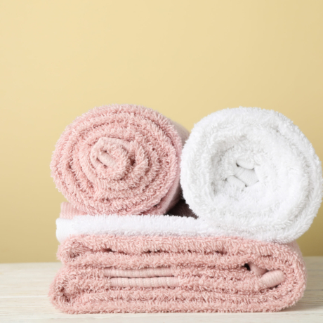 Folded towels on white wooden table against beige background, sp